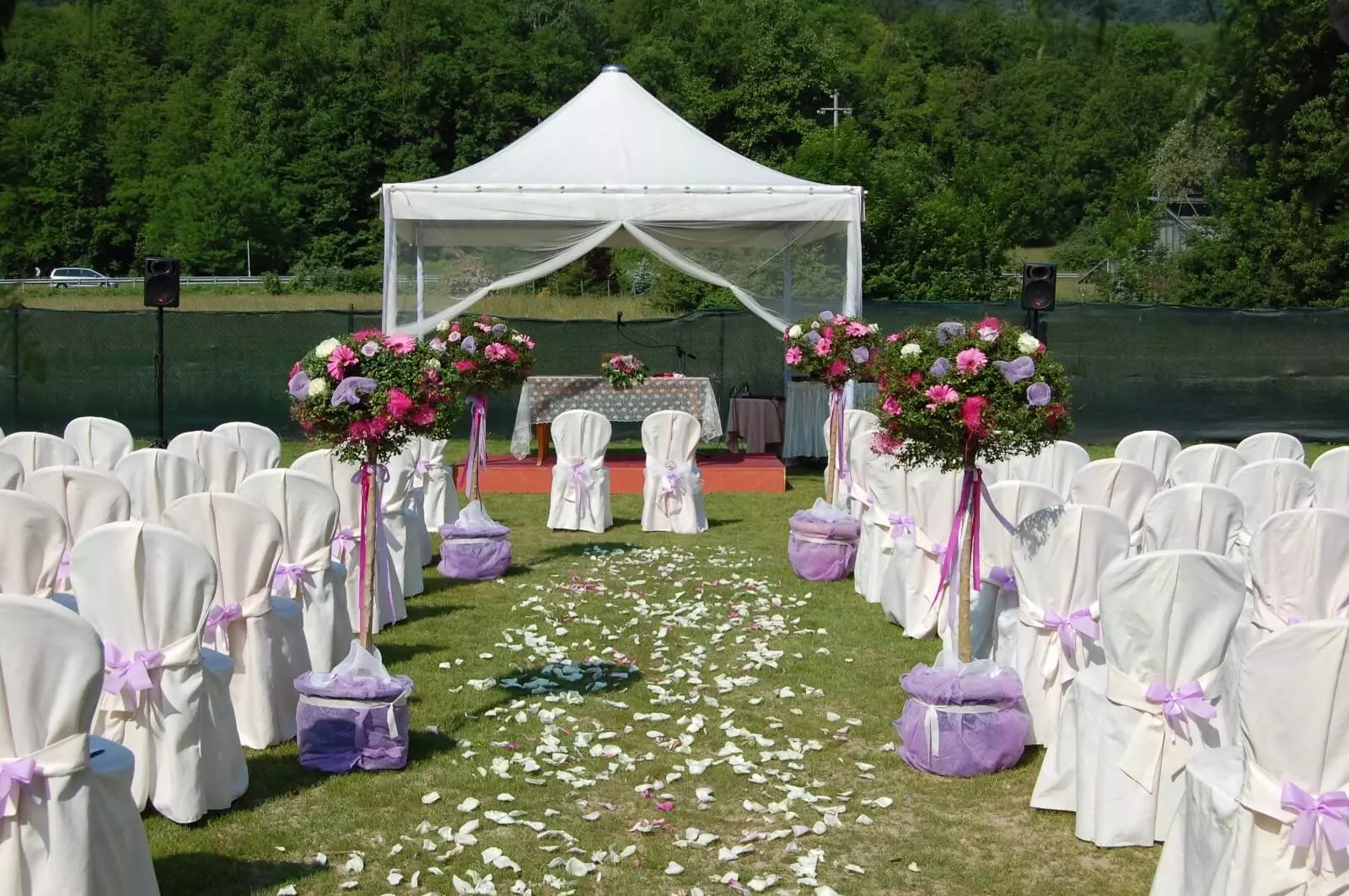 matrimoni-in-villa-puccini-ai salici Scenario di un matrimonio ai Salici, con navata nel prato e petali di rosa per terra. Ai lati le sedie bianche per gli ospiti e in fondo il gazebo per gli sposi